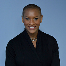 Claudia Gordon, an African-american woman with short dark hair smiles at the camera. She is nicely dressed in a floral skirt and black blouse.